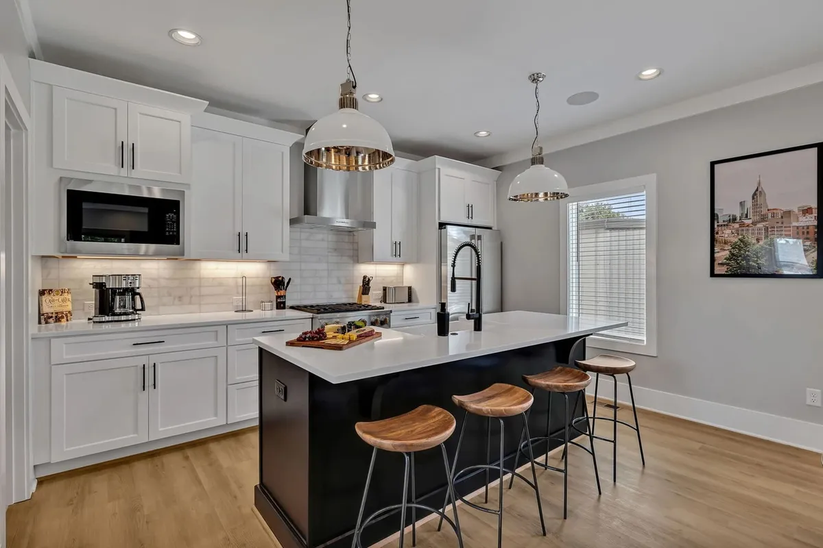 A sleek kitchen with an island countertop, bar stools, Monogram stainless-steel appliances, and modern wall art. The setup invites both cooking and casual interaction, with plenty of space for guests to mingle or enjoy a snack at the bar.