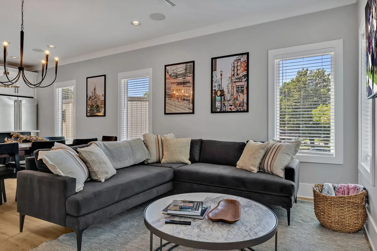 The image showcases a beautifully styled living room with a plush sofa, elegant coffee table, and vibrant artwork adorning the walls. The space feels inviting and is perfect for relaxing, sharing stories, or gathering with friends and family. Designer touches and cozy lighting create a warm, upscale atmosphere ideal for group getaways.
