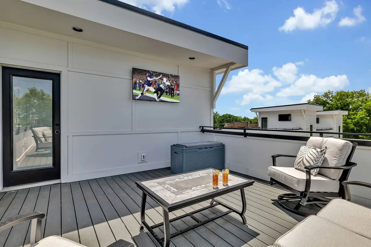 An inviting outdoor seating area with a TV screen, coffee table, and comfortable seating, perfect for relaxing or socializing with friends. The scene is set for outdoor entertainment, such as watching a live game or enjoying drinks at sunset.