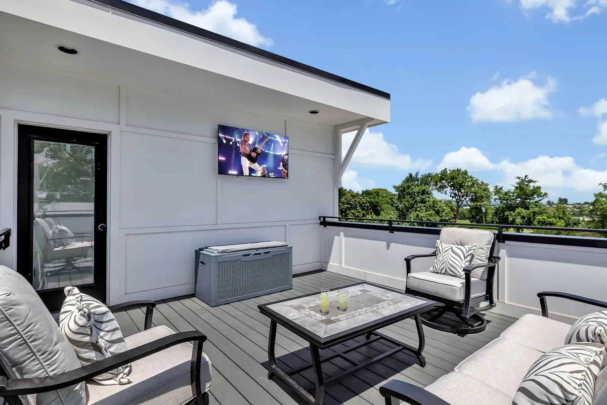 Pictured here is an outdoor seating area on a rooftop, complete with a television, coffee table, and planters accenting the space. The setting is lively and casual, suggesting an ideal environment for entertaining guests, watching the sunset, or enjoying a sports event under the sky.
