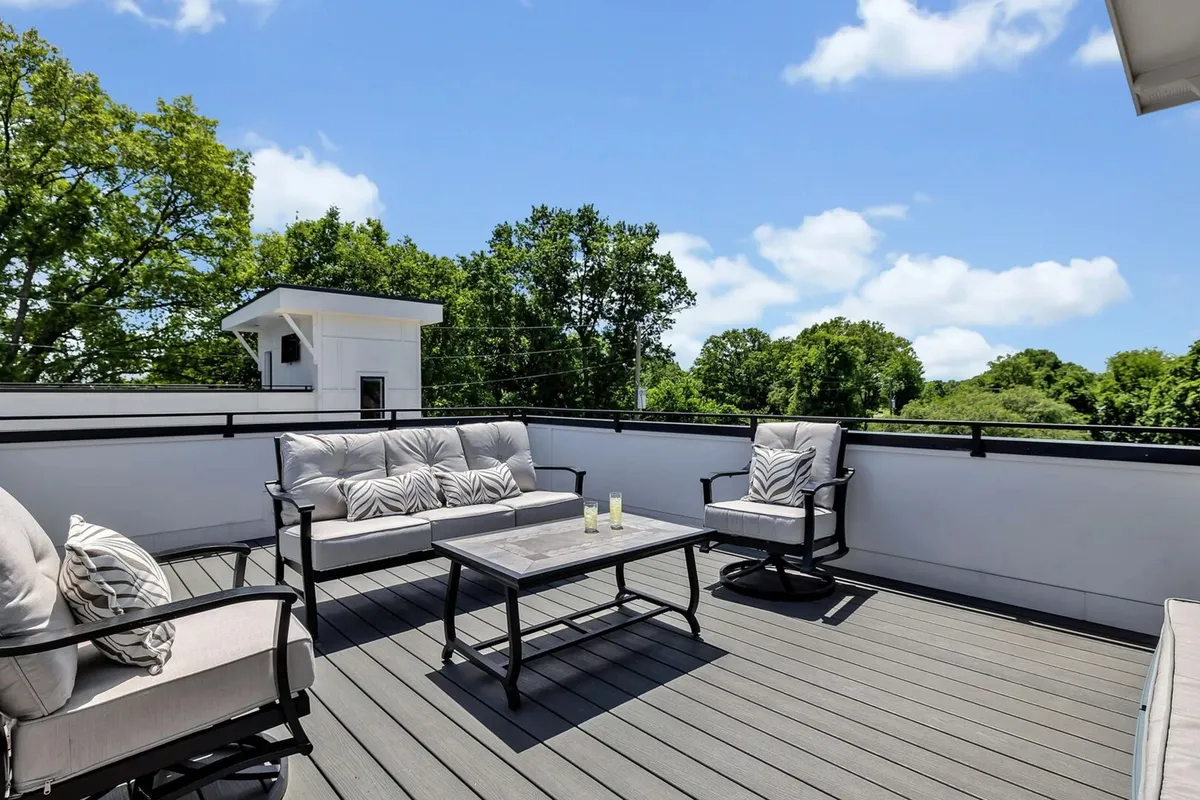 This image features a comfortable outdoor seating arrangement with a decorative table, set against a lush backdrop of green trees. The space invites relaxation and socializing, evoking the feel of a private retreat while remaining connected to the outdoors.