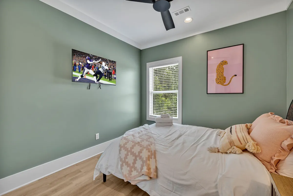 A cozy and playful bedroom with a queen-sized bed dressed in decorative pillows, a TV mounted on the wall, and colorful artwork above. The space radiates comfort and is ideal for relaxation or catching up on favorite shows.