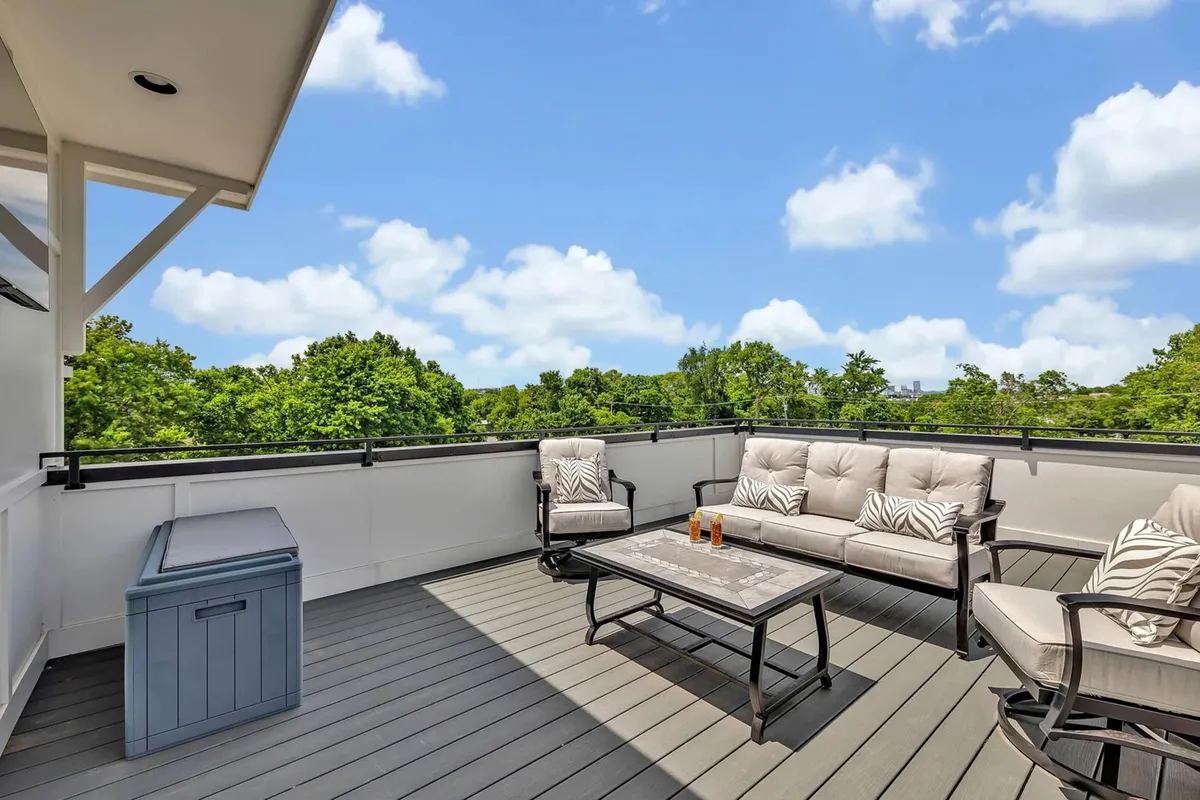 A tranquil rooftop deck with comfortable seating, a coffee table with drinks, and a lush green view—ideal for relaxing, entertaining guests, or enjoying sunset cocktails after a day of exploration.