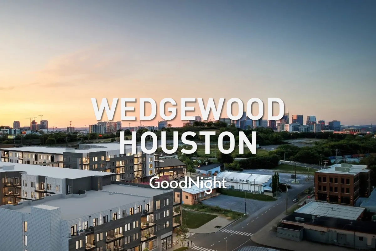 A vibrant exterior scene featuring modern apartment buildings set against a colorful sunset sky. The city skyline frames the background, while pedestrians can be seen leisurely walking and enjoying the local ambiance, hinting at the area's lively nightlife and accessibility to dining and entertainment options.